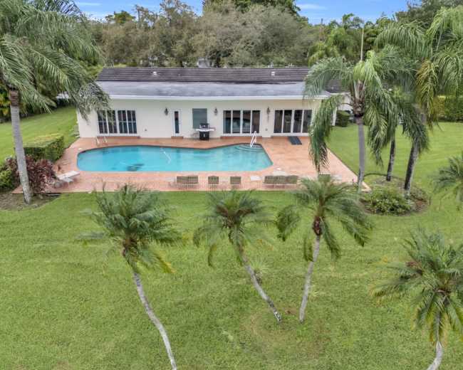 A house with a swimming pool surrounded by palm trees is visible in a landscaped yard.