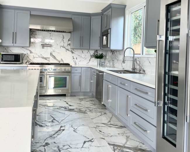 The kitchen features gray cabinetry, a stainless steel refrigerator, a marble backsplash, and a tiled floor.