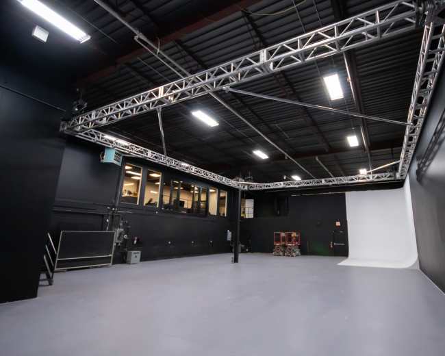 The image shows an empty photography studio with black walls, a gray floor, and a white backdrop at one end.