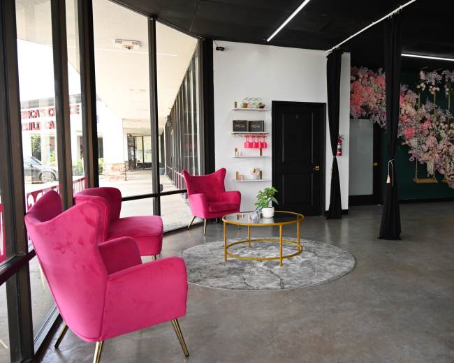 A modern interior features two pink armchairs, a round gold coffee table, and a decorative wall with floral designs.