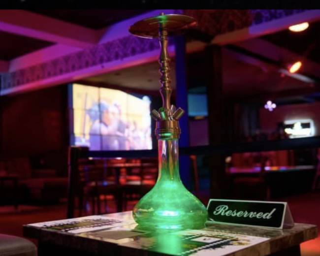 A lit hookah is placed on a table marked "Reserved" in a dimly lit lounge with a projection screen in the background.