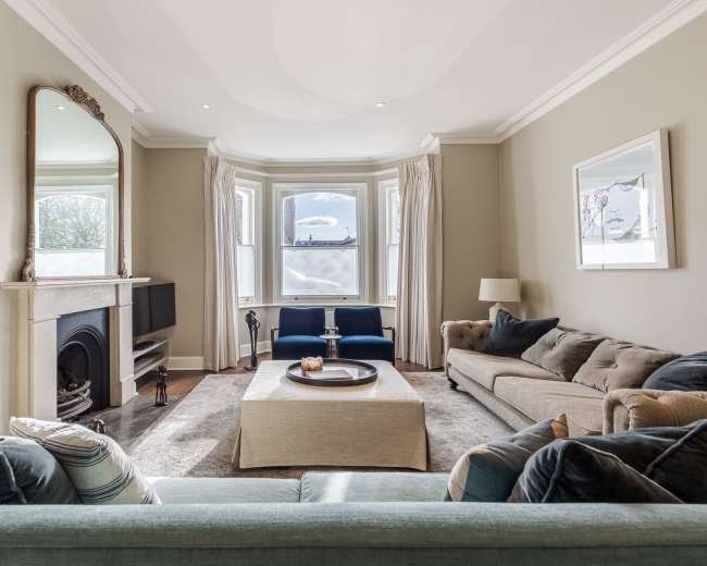 The living room features a large window with a view, a fireplace, a sofa, two blue chairs, and a coffee table in the center.
