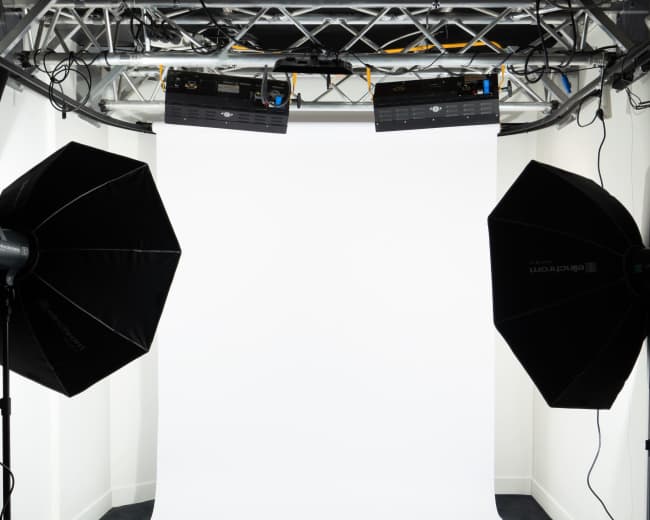 The image shows a photography studio setup featuring two light sources directed at a white backdrop.