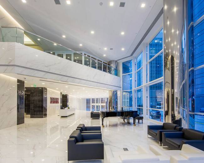 The image shows a spacious, modern lobby with marble floors, large windows, and contemporary furniture, including a grand piano.