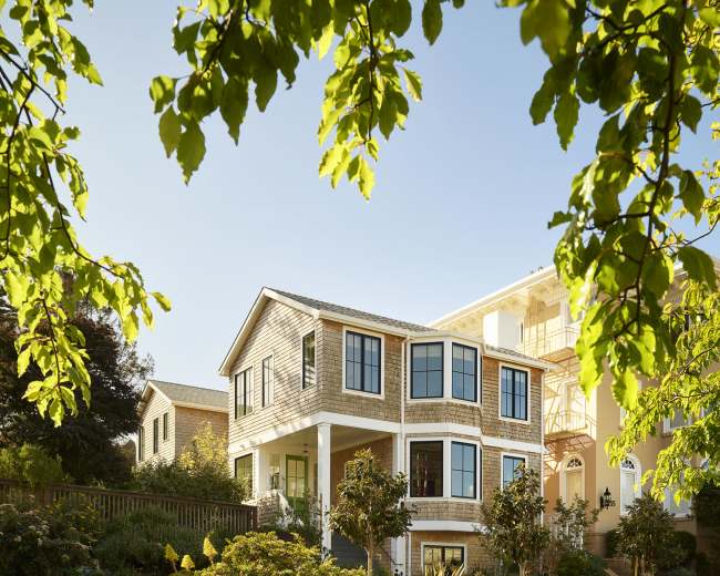 A modern two-story house with large windows is surrounded by landscaped gardens and trees.