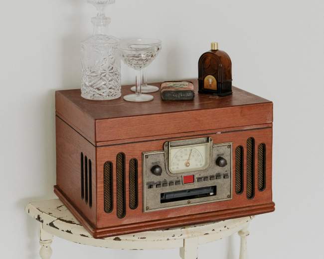 A vintage wooden radio sits on a small table, accompanied by a crystal decanter, a glass, and a decorative bottle.