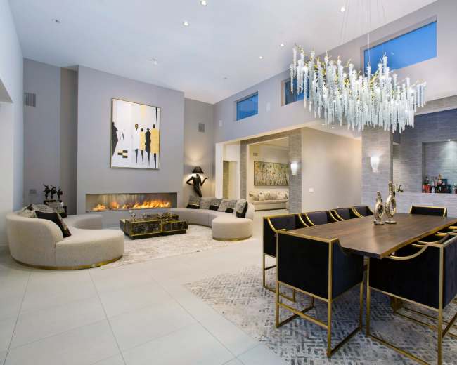 The image shows a modern open-concept living and dining area with a chandelier, decorative artwork, and a fireplace.
