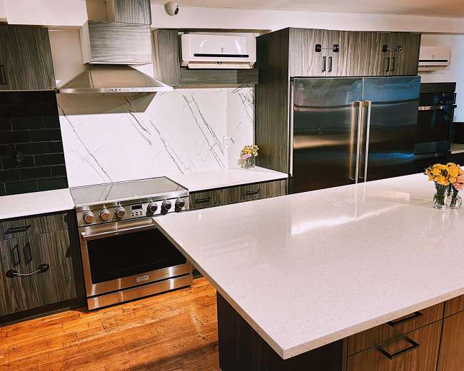 A modern kitchen with dark wood cabinetry, stainless steel appliances, a large island with a quartz countertop, and a floral centerpiece.