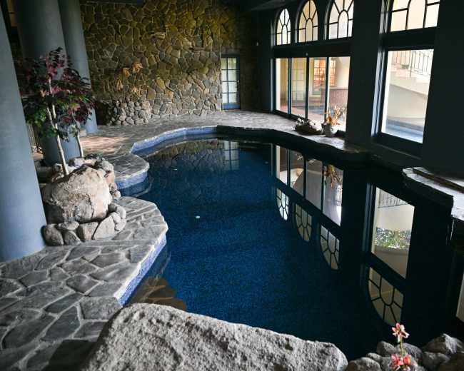The image shows a stone-enclosed indoor pool area with large windows and a smooth, tiled floor.