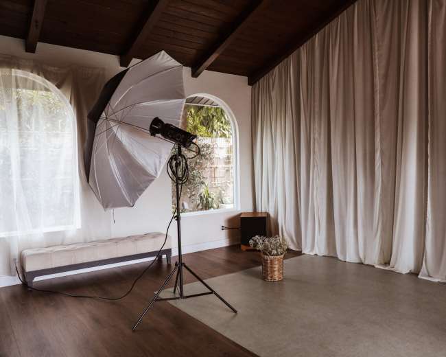 A photography studio with a large umbrella softbox, a woven basket of flowers, and draped white curtains against a wooden ceiling.