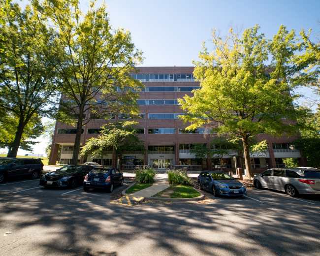 A multi-story brick building is surrounded by trees and parked cars in a well-lit area.