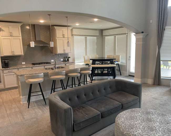 The image shows a modern open-concept living space that includes a kitchen with bar seating, a dining area with a table, and a comfortable seating area.