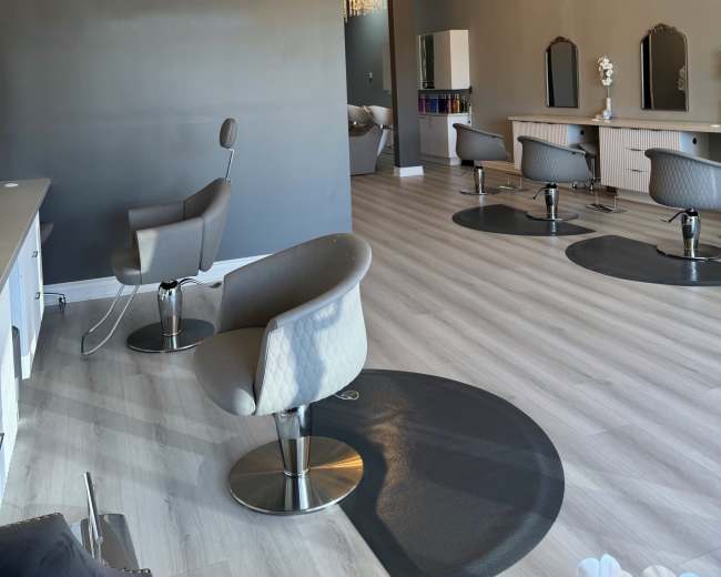The image shows a modern salon interior with several styling chairs, mirrors, and chandeliers, all set against a gray wall featuring a large "IM" logo.