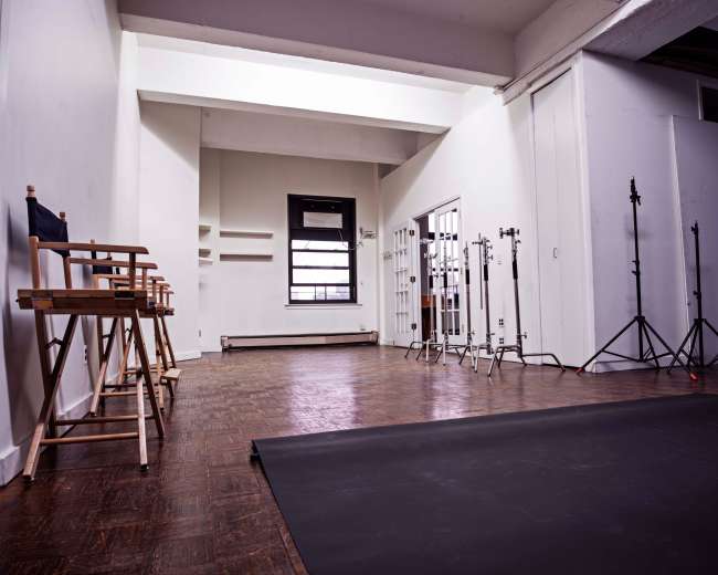 A spacious, empty studio with wooden flooring, equipped with director's chairs and lighting stands.