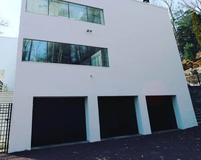 A modern three-garage structure with large windows and a smooth exterior wall, situated among trees.