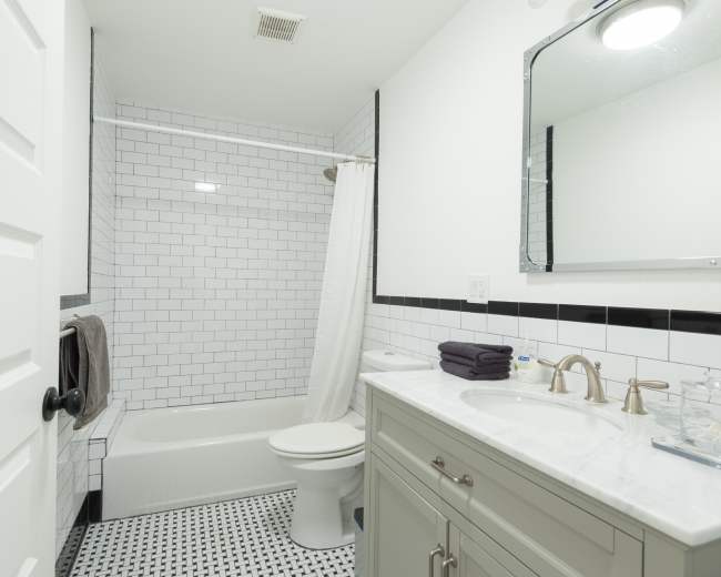 The image depicts a modern bathroom featuring a shower and bathtub combo, a vanity with a sink, and black-and-white tiled flooring.