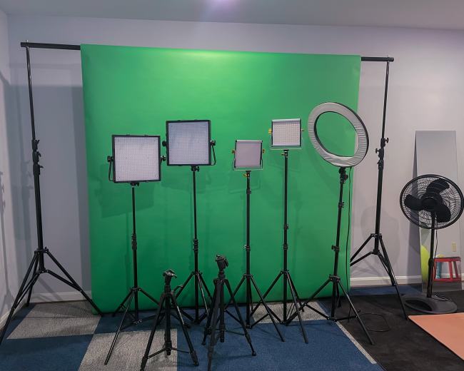 The image shows a green backdrop setup for video or photography, with multiple lighting fixtures positioned on stands.