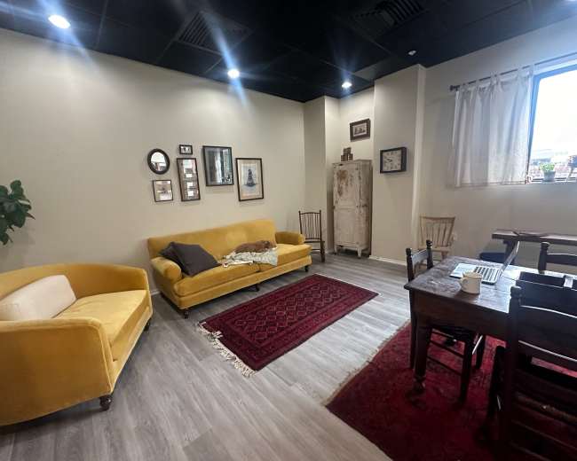 A cozy room features a yellow couch, a wooden dining table with chairs, and various framed pictures on the walls.