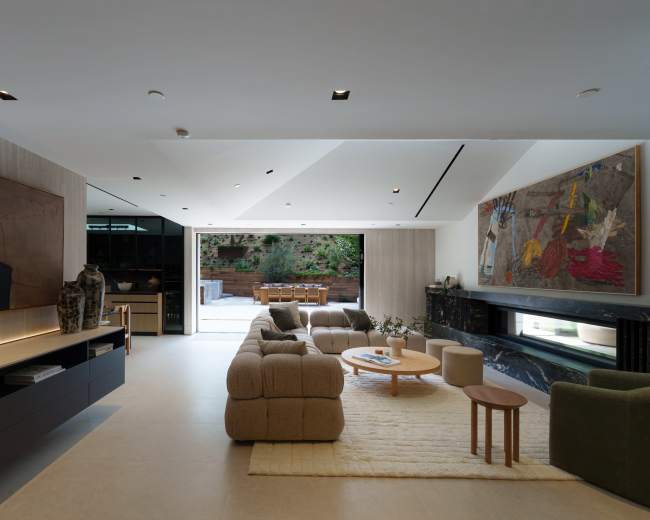 The image shows a modern living room with a large sectional sofa, two abstract paintings on the walls, and a glass door leading to an outdoor patio area.