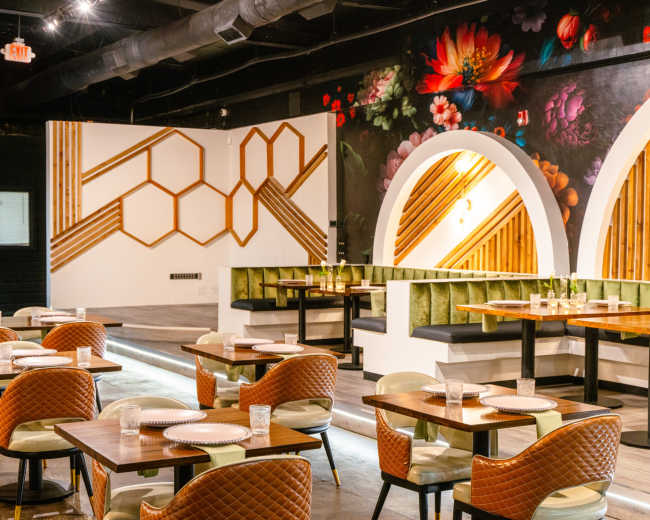 The image shows a modern restaurant interior featuring wooden hexagonal designs on the walls, green upholstered seating, and tables set with plates and glasses.