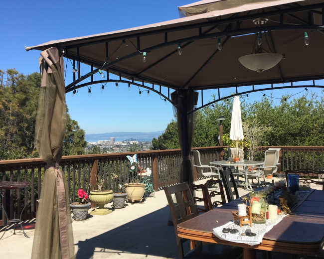 A covered outdoor seating area with a table and chairs overlooks a city view under a clear blue sky.