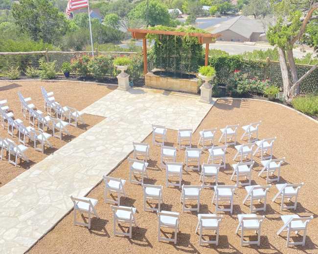 A row of white chairs is arranged on a stone pathway for an outdoor event, overlooking a green landscape with a flagpole in the background.