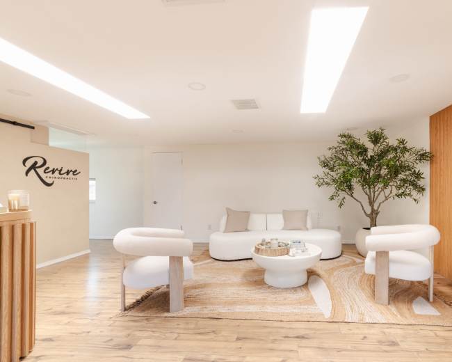 A modern lounge area features a circular white sofa, two curved chairs, and a round coffee table, surrounded by a decorative rug and a potted plant.