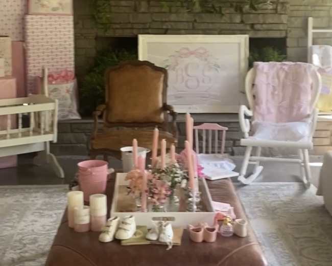 A cozy room with a mix of decorative elements, including a leather coffee table, a vintage chair, baby furniture, and pink-themed decor against a stone wall.