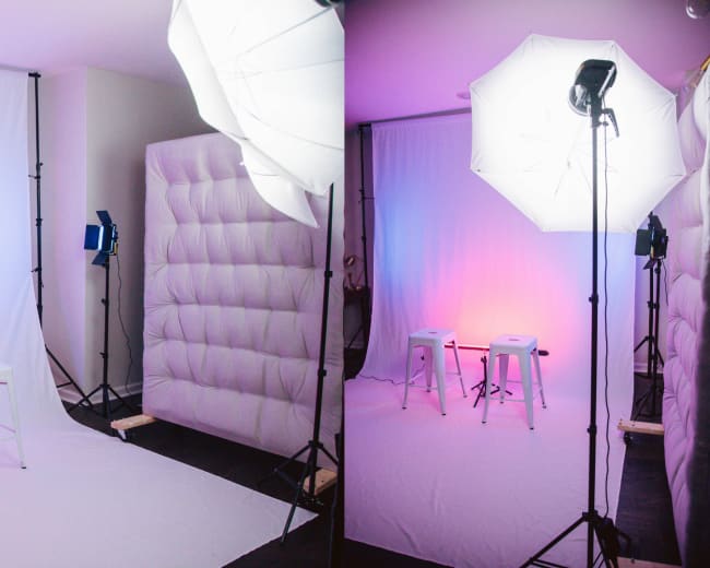 The image shows a photography studio setup with two stools placed in front of a plain backdrop, illuminated by softbox lights on either side.
