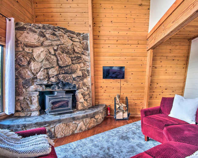 A cozy living room featuring a stone fireplace, a red upholstered sofa, and wooden walls.