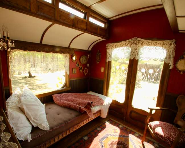 The image shows a cozy interior of a vintage-style room with lace curtains, a daybed, and ornate decorations.