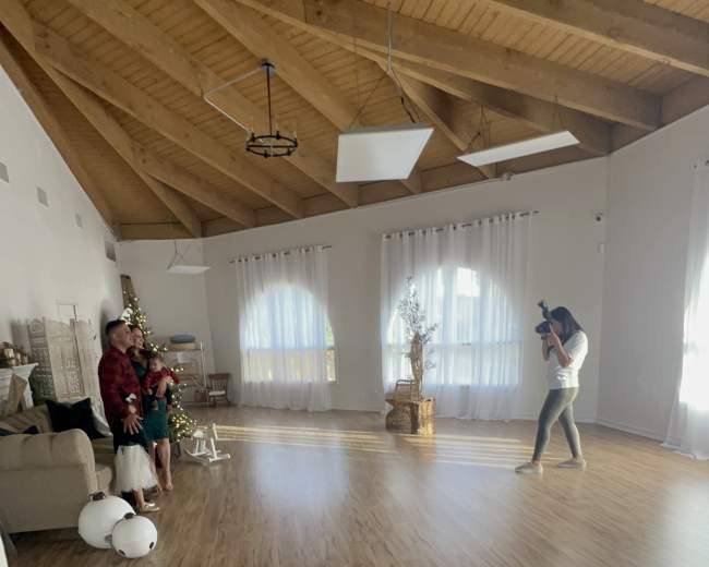 A spacious room with wooden beams, large windows, and a photographer capturing a family posed near a Christmas tree.