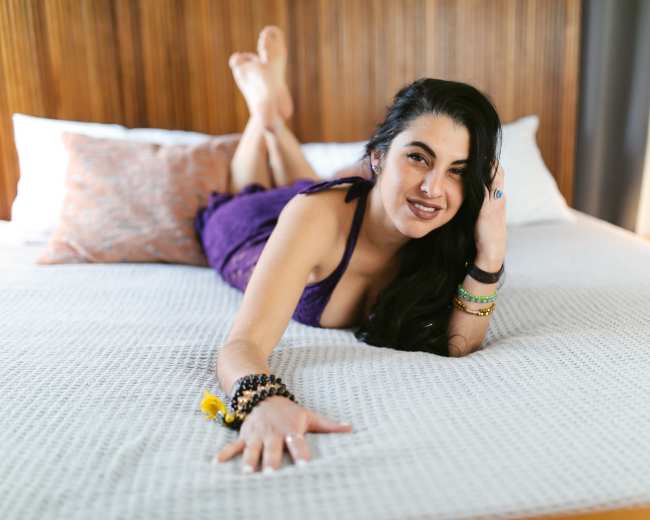 A woman lies on a bed, propped on her elbows with her legs extended behind her.