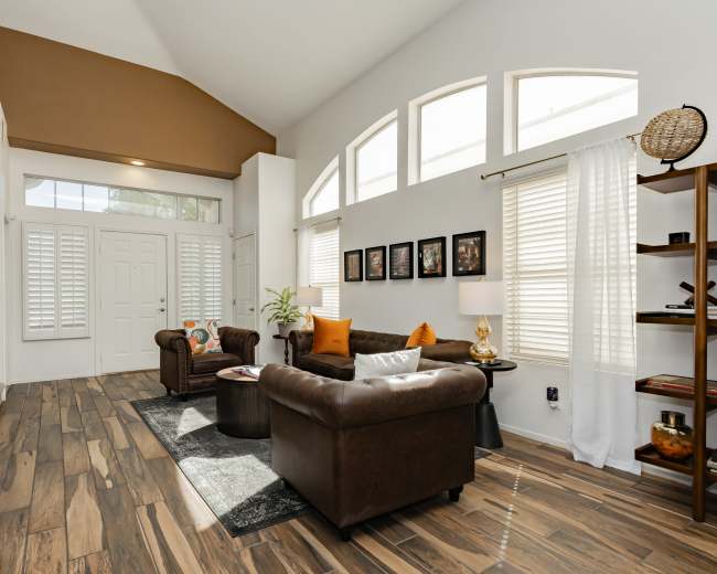 The living room features a high ceiling, large windows with sheer curtains, and leather furniture arranged around a coffee table.