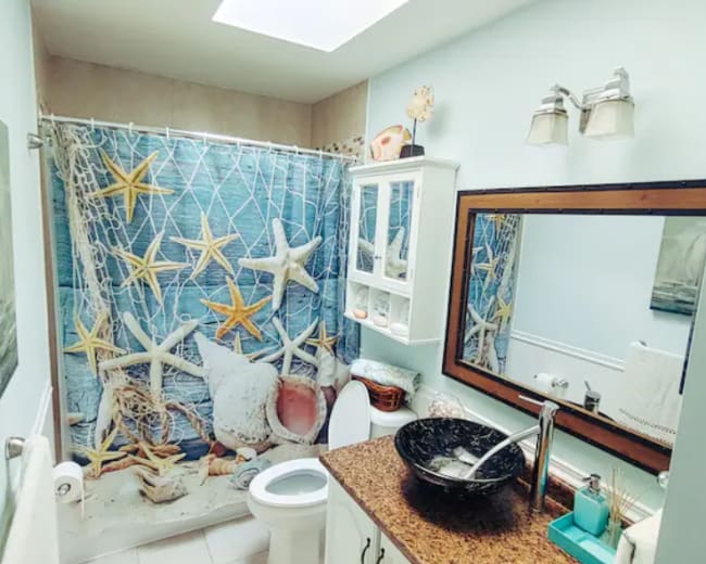 The image shows a bathroom with a blue and white starfish-themed shower curtain, a granite countertop sink, and a large mirror above it.