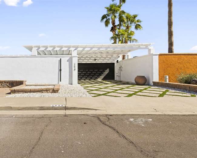 A modern home entrance with a carport, a landscaped area with gravel and grass, and a stone seating area beside the street.