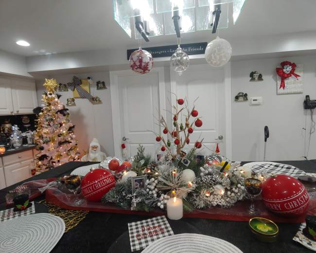A decorated dining table with a festive centerpiece, surrounded by holiday decorations, a Christmas tree, and various ornaments.