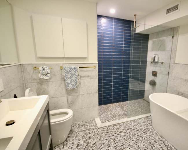 The image shows a modern bathroom featuring a glass shower, a freestanding bathtub, and marble tile flooring.