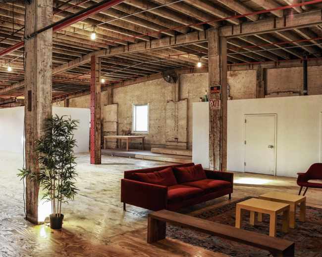 A spacious, industrial-style interior with wooden beams, a red couch, a yellow coffee table, and a large open area.