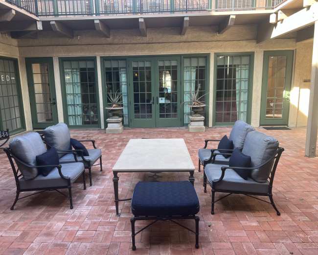 A courtyard features a set of four armchairs and a coffee table arranged on a brick floor, with large green-paneled windows in the background.