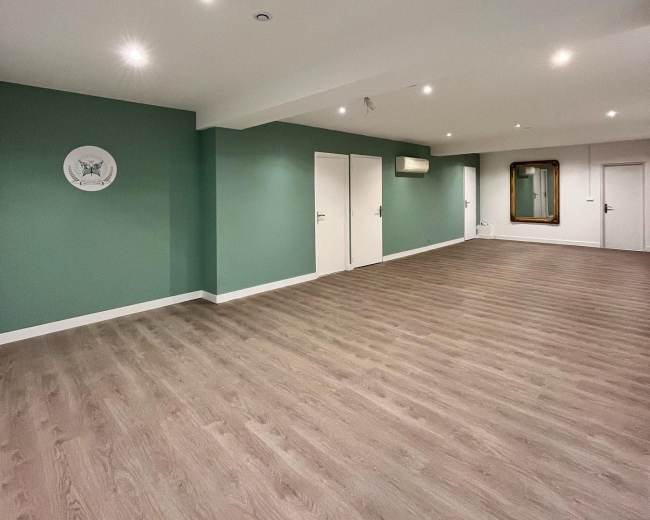 The image shows a spacious, empty room with green accent walls, hardwood flooring, recessed lighting, and two closed doors.