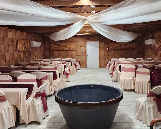 An indoor venue with rows of tables covered in white tablecloths and burgundy accents, a large black basin in the center, and draped fabric on the ceiling.