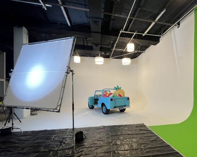 A light blue car filled with inflatable beach toys is positioned in a studio with a white backdrop and lighting setup.