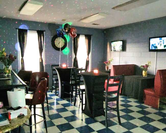 A dimly lit room with checkered blue and white flooring, featuring several tables, chairs, and decorations including balloons and flower arrangements.