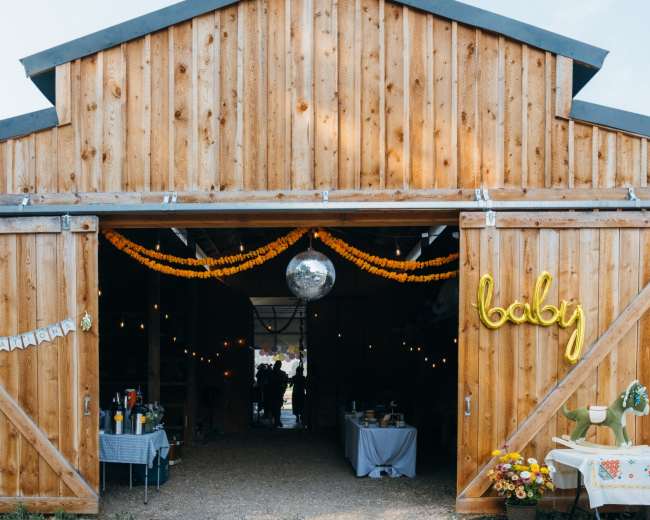 A wooden barn with an entrance adorned with yellow decorations and a disco ball hangs inside.