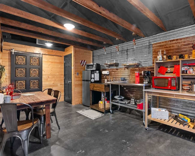 The image shows a rustic kitchen and dining area featuring a wooden table, modern appliances, and a metal accent wall.