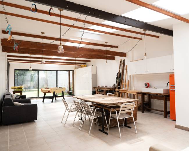The image shows a spacious, modern living area with a wooden dining table, metal chairs, and a large glass door leading to an outdoor space.