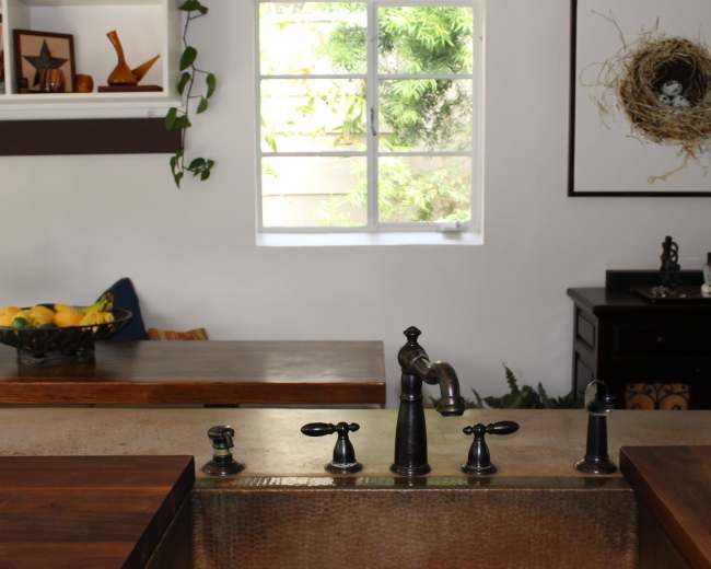 A kitchen with a sink and multiple faucets, set against a backdrop of a window and wooden countertops.