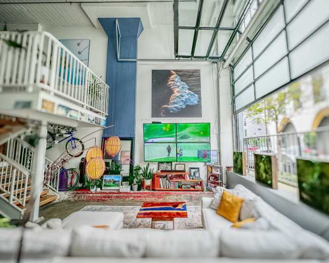 A spacious, modern living room with a large sectional sofa, a mounted television displaying a golf game, and artwork on the walls.