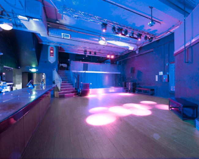 The image shows a spacious nightclub interior with a bar area, a dance floor, and stage lighting effects.